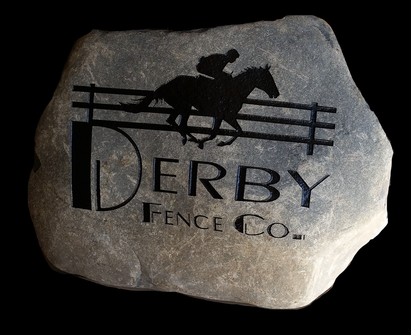 A large rock with an engraved black silhouette of a horse and rider jumping over a fence. Below the image, the text reads "Derby Fence Co.